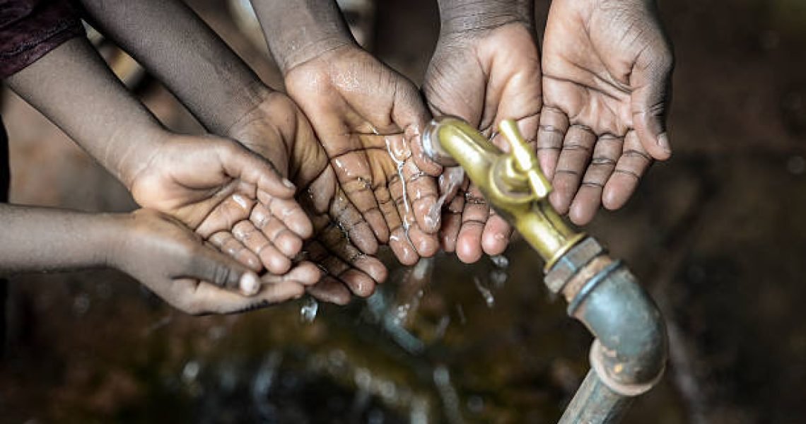 Three African children with their hands cupped under a water tap.